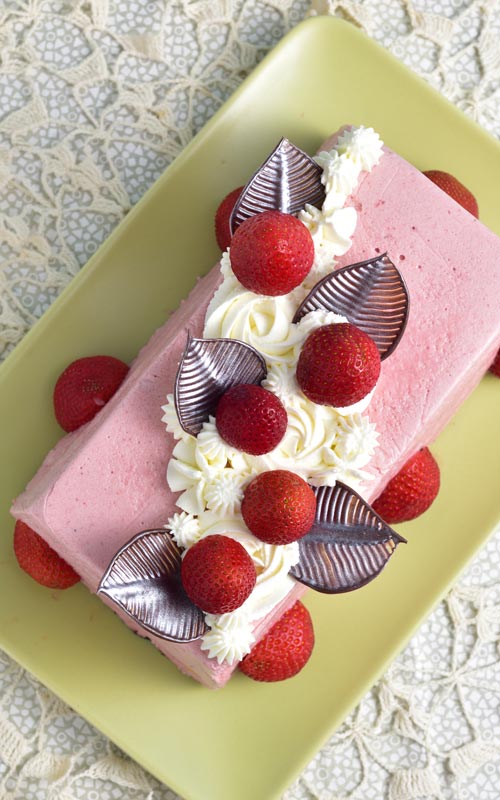 Strawberry mousse cake decorated with chocolate leave and whipped cream swirls.