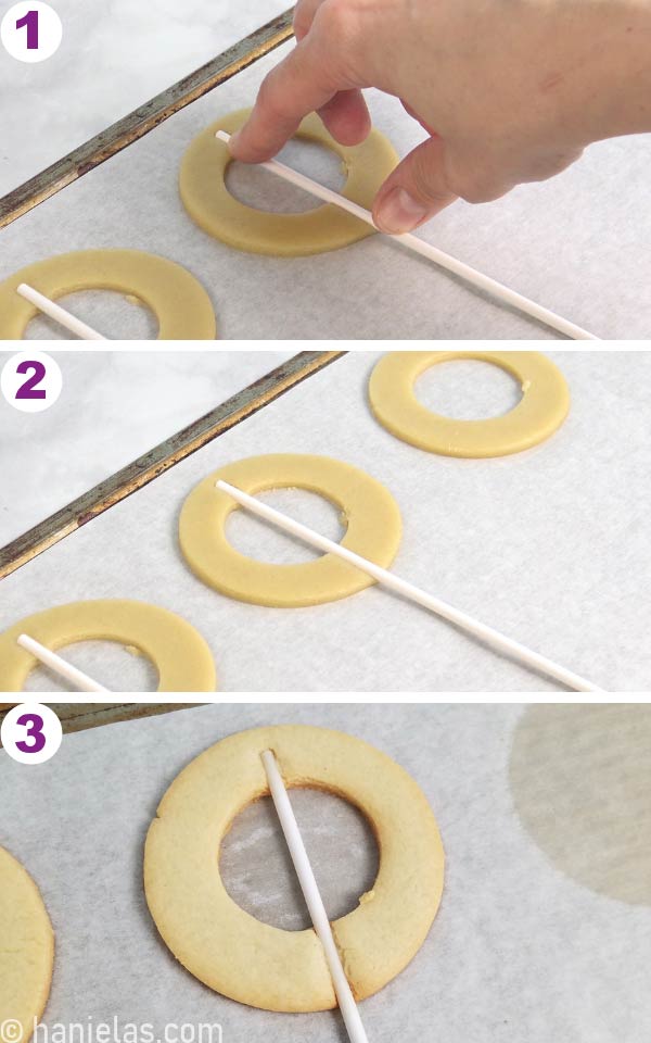 Cookie on a baking sheet, hand pressing a lollipop stick on top of the cookie.