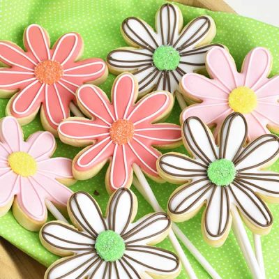 Decorated daisy flower cookies on a wood tray lined with bright green cloth.