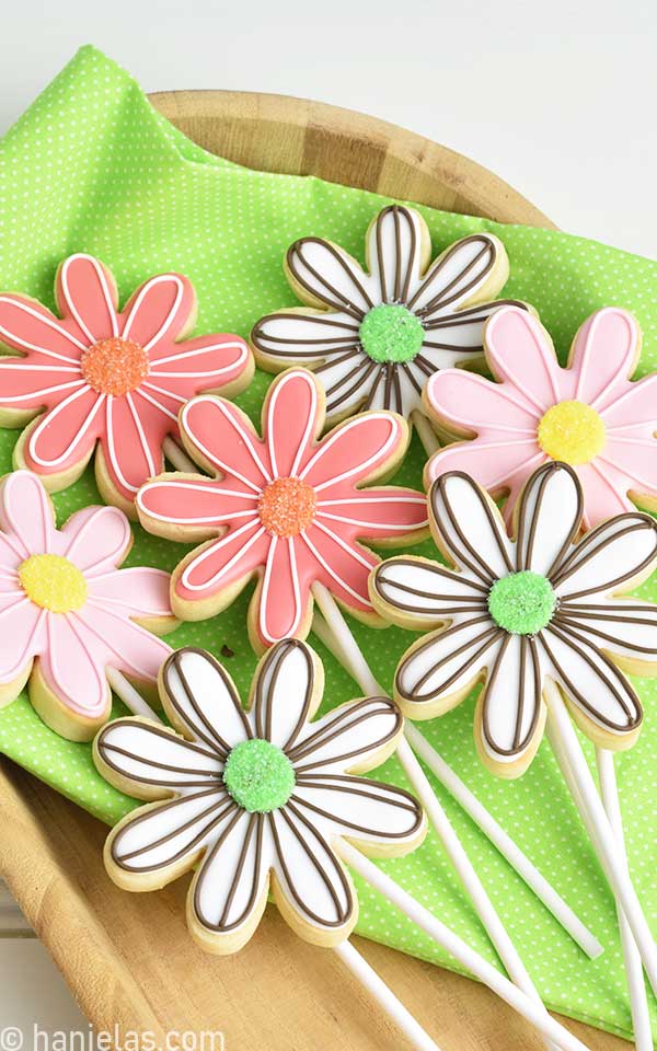 Decorated daisy flower cookies on a wood tray lined with bright green cloth.