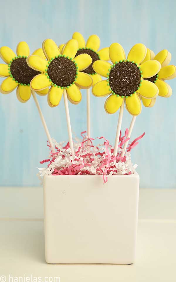 Sunflower cookies on a stick displayed in a white vase.