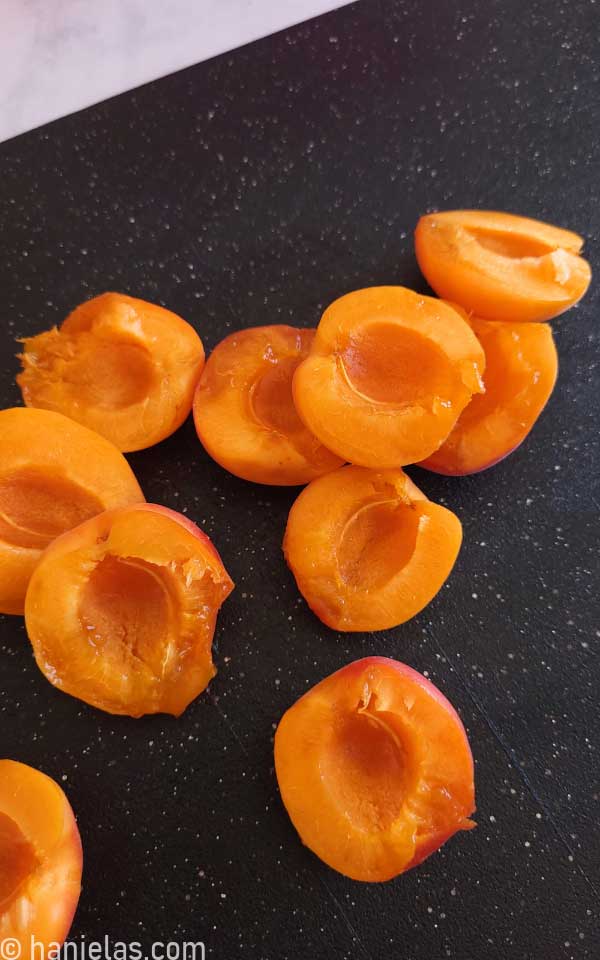 Fresh apricots sliced and stones removed on a black cutting board.