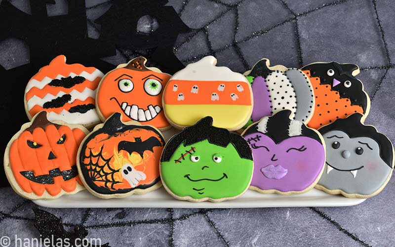 Decorated pumpkin Halloween cookies displayed on white rectangular plate.