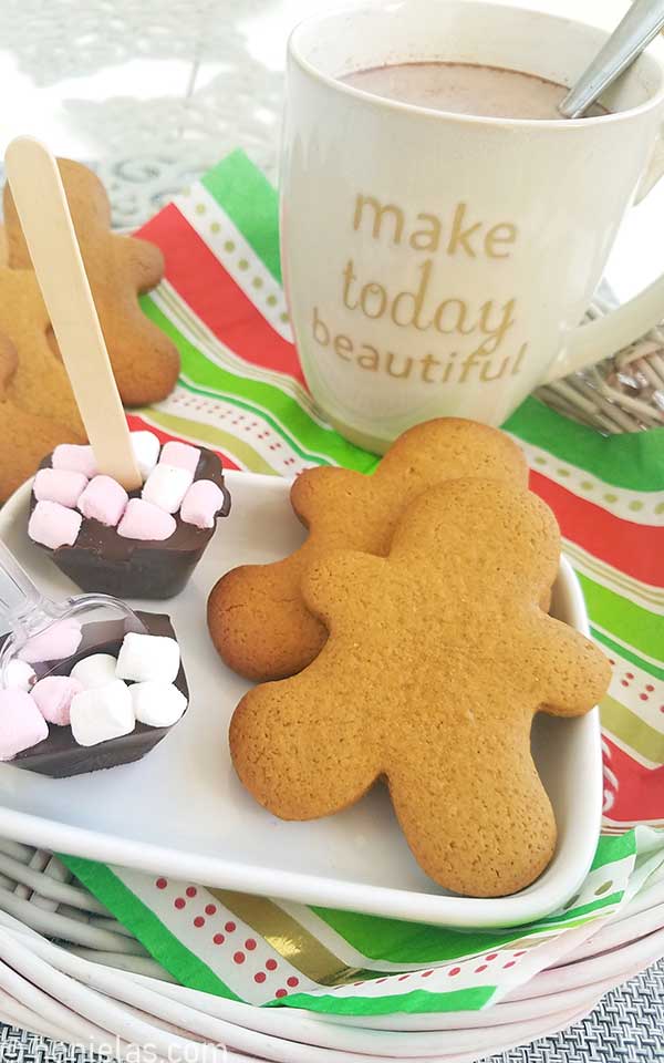 Baked gingerbread men cookies on a white plate with hot chocolate.