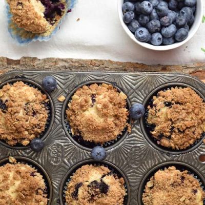 Baked muffins in a pretty muffin tin, fresh blueberries in small bowl.