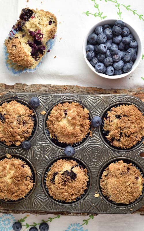 Baked muffins in a pretty muffin tin, fresh blueberries in small bowl.