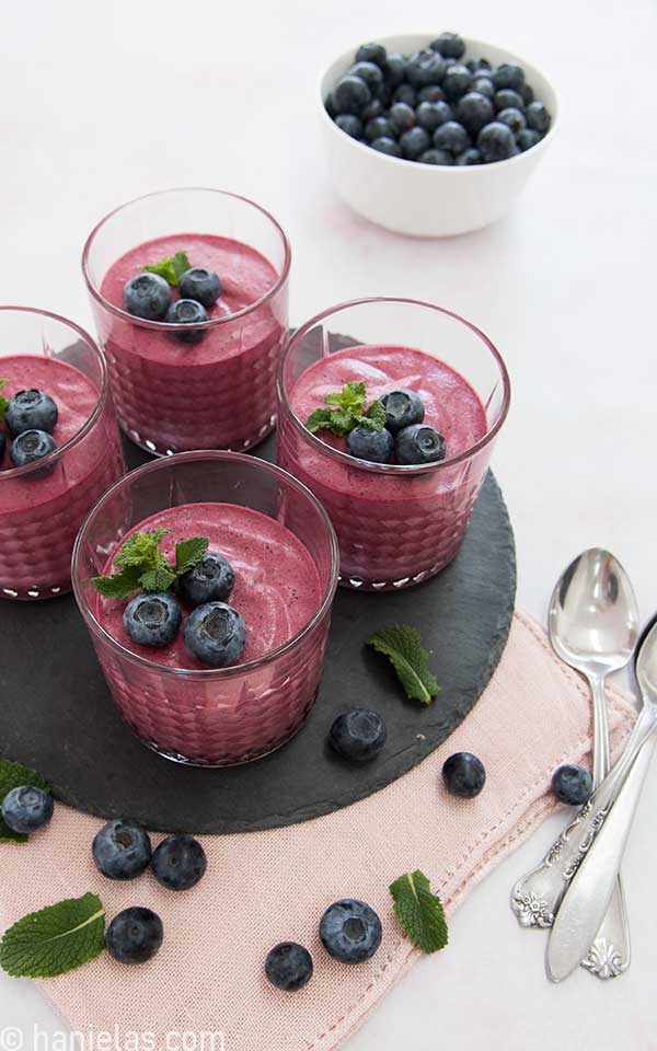 Four glasses with bright purple mousse set on a black tray.