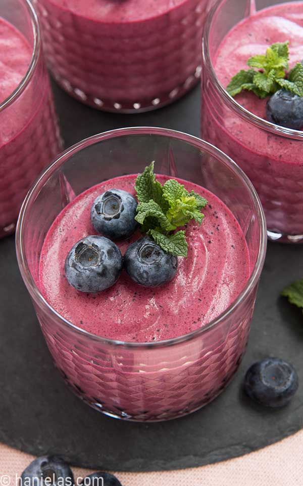 Bright purple mousse in a glass, garnished with three fresh blueberries and mint leaves.