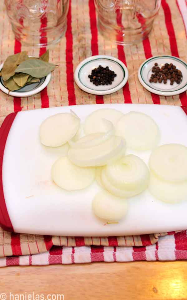 Three small dishes with bay leaves, allspice and black pepper, and a cutting board with sliced onion.