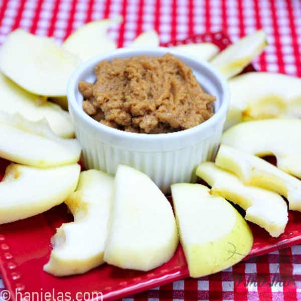 Apple slices arranged, on a plate, around a ramekin filled with a dip.