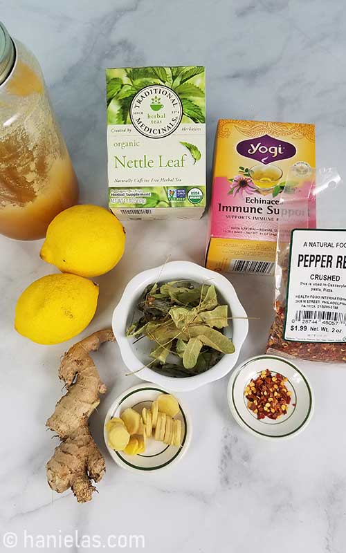 Ginger root, lemon, dry tea leaves, honey and chili flakes on a table.