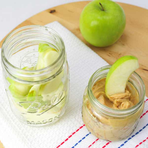 Two glass jars, one filled with apples, and second one with a dip.