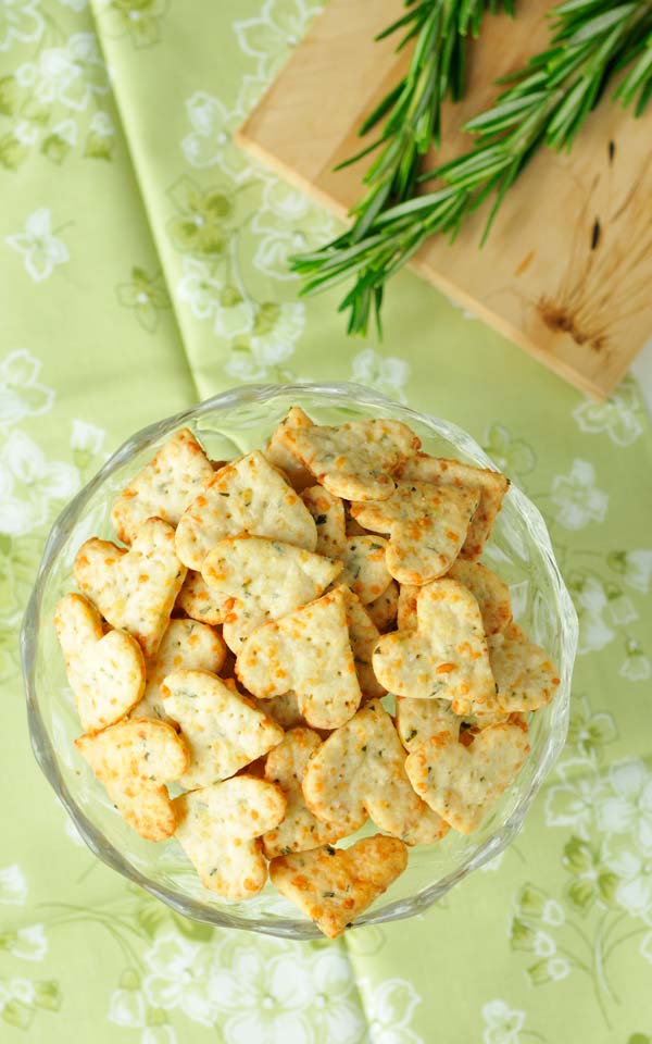 A bowl full of heart-shaped crackers is seen from above, with fresh rosemary on the side.