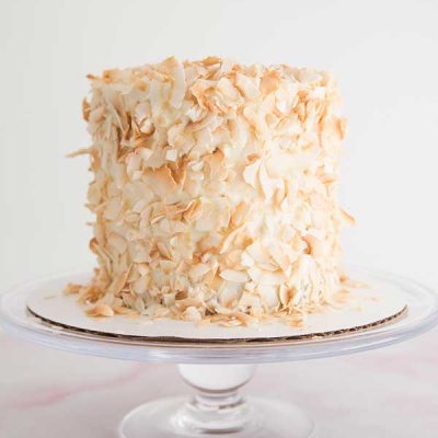 Cake decorated with toasted coconut flakes on a cake stand.