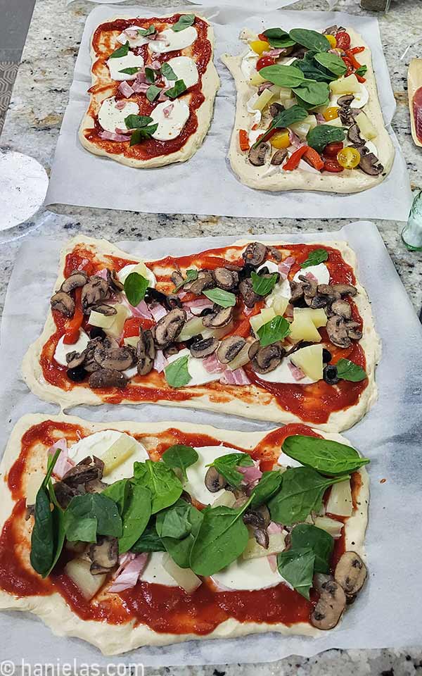 Rectangular pizzas with toppings on a counter.