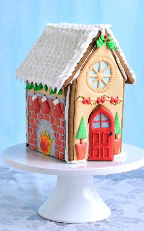 Decorated gingerbread house displayed on white round cake stand.