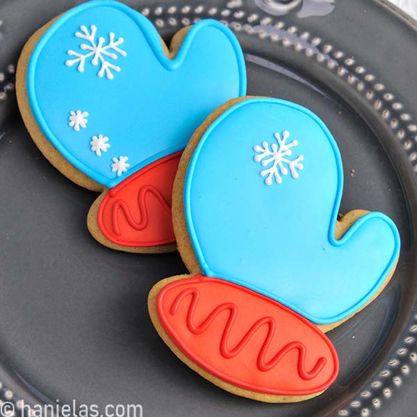 Mitten cookie decorated with blue and red icing on a gray plate.