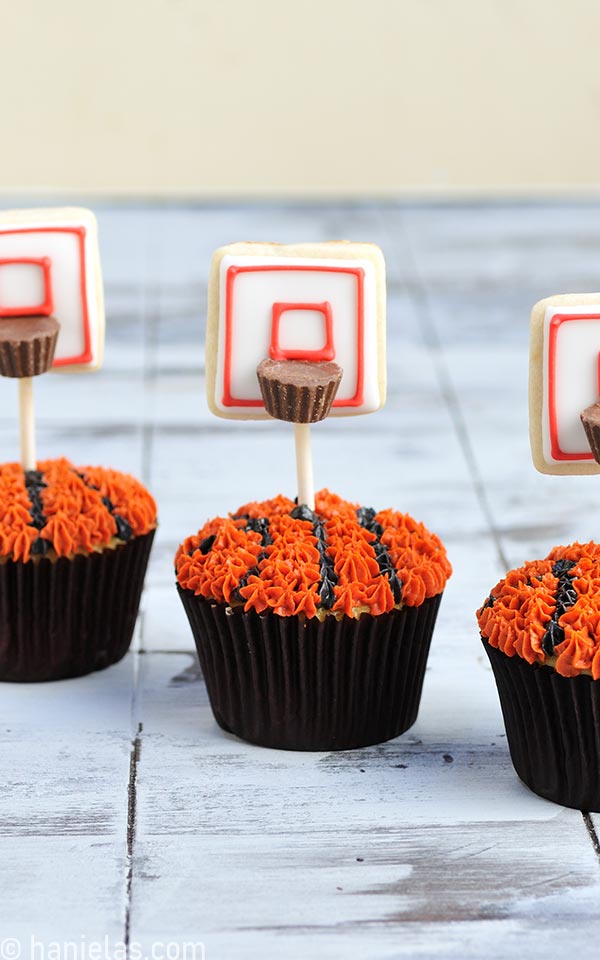 Cupcakes in brown liners decorated with buttercream and cookie pops.