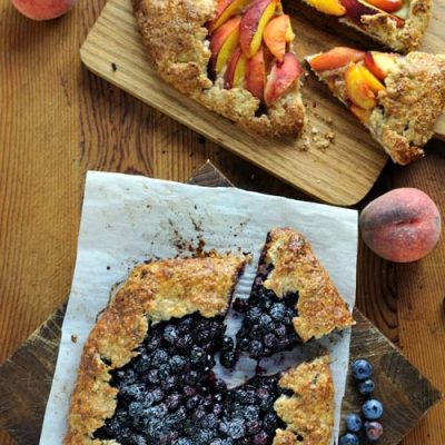 Sliced peach and blueberry free form tarts on wooden cutting boards..