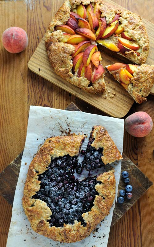 Sliced peach and blueberry free form tarts on wooden cutting boards..