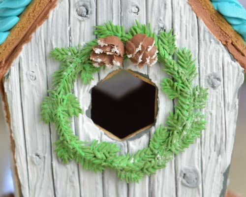Detail of royal icing wreath attached on a gingerbread house.