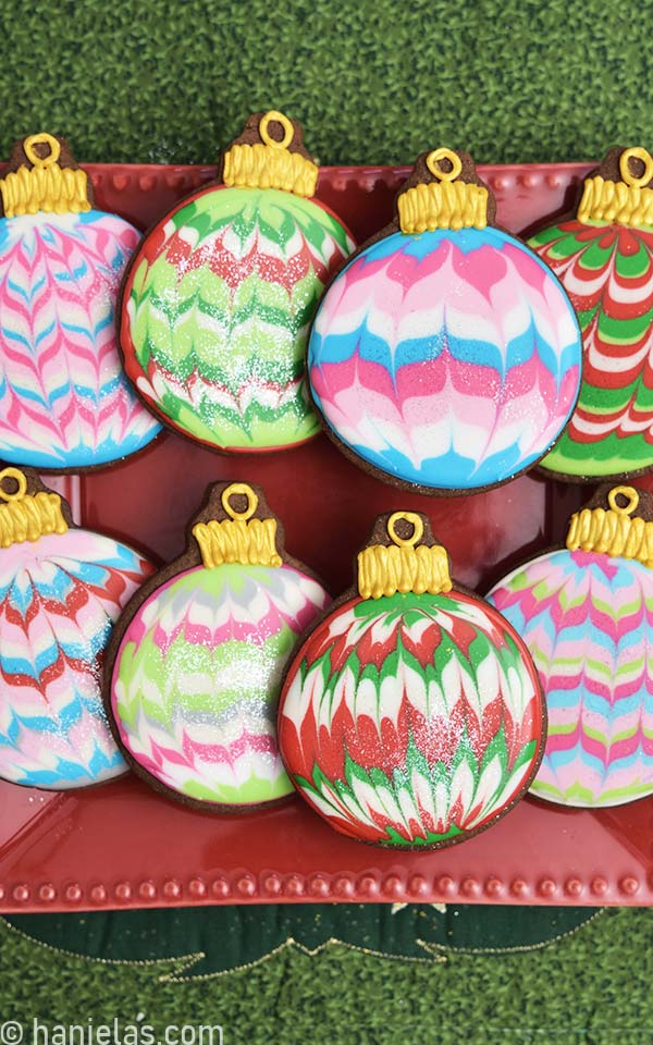 Chocolate cookies shaped like round Christmas ornaments decorated with marbled royal icing displayed on a red plate.