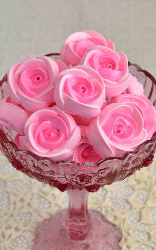 Pink meringue rose cookies in a pink glass bowl.