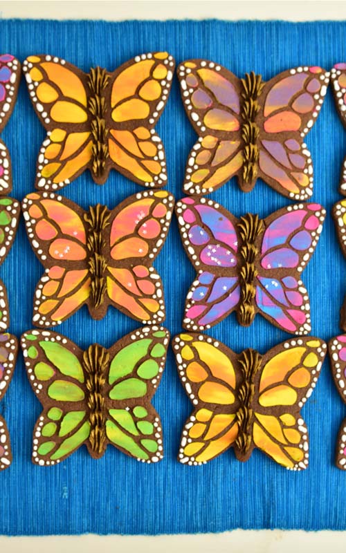 Chocolate butterfly cookies stenciled with royal icing on a blue tablecloth.
