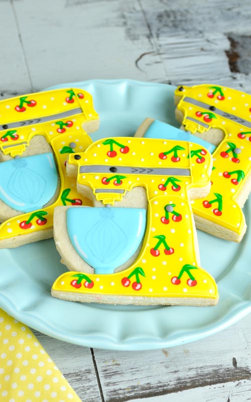 Yellow stand mixer cookies with cherry pattern on a blue plate.