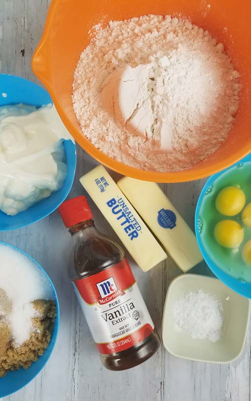 Flour, broken egg, butter, sugar baking powder in bowl and vanilla extract bottle and stick of butter.