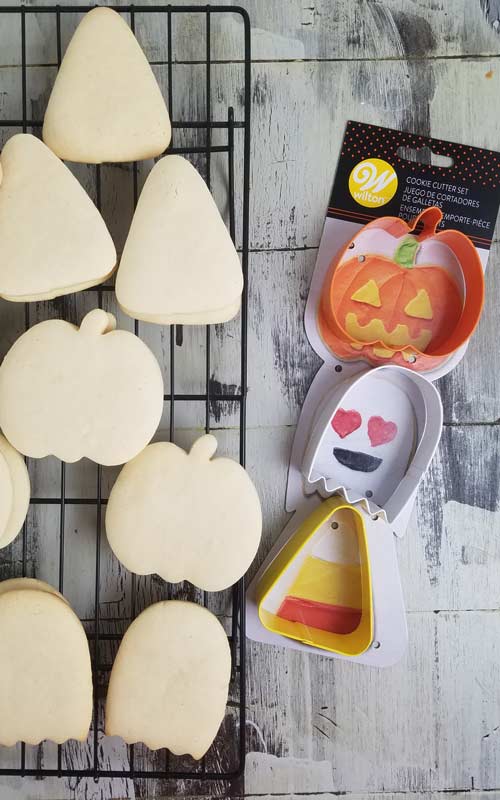 Baked cookies on a cooling rack along with halloween cookie cutters used to cut them out.