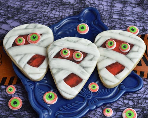 Decorated mummy cookies displayed on a dark blue square plate.