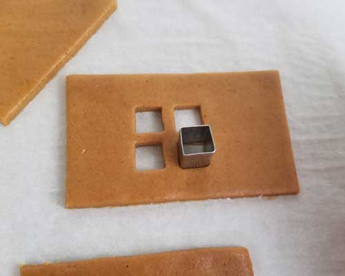 Cutting out a small window from a cookie dough using a mini square cutter.