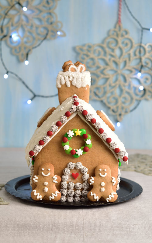 Candy decorated gingerbread house on a black plate.