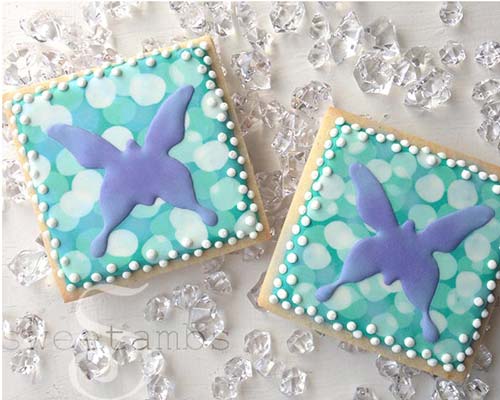 Decorated butterfly cookies on a white background surrounded by clear gems.