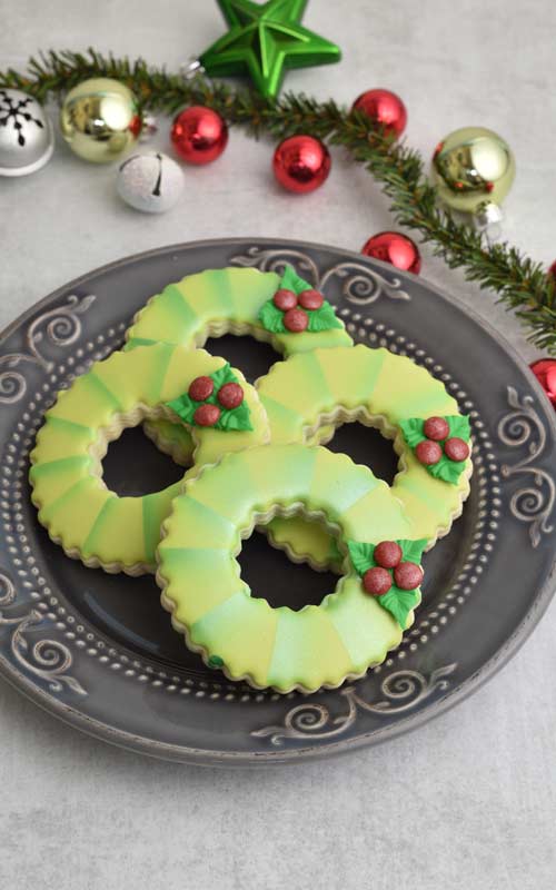 Decorated cookies shaped like wreath displayed on a plate.