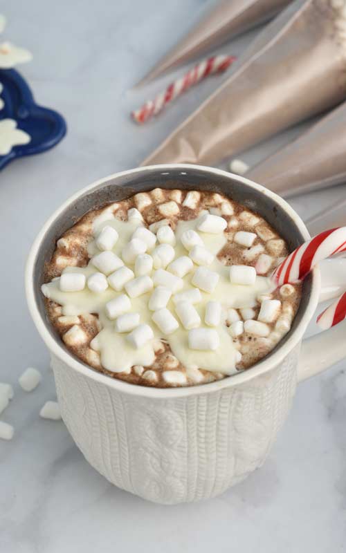 Mug filled with hot cocoa topped with chocolate snowflake and marshmallows.