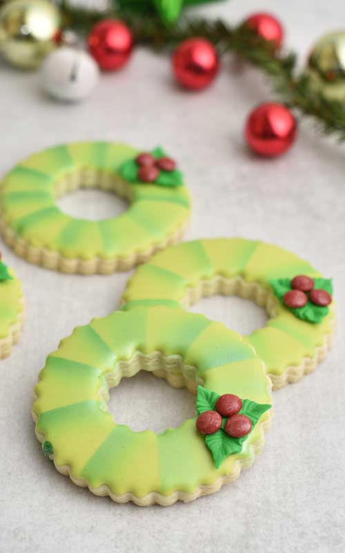 Royal icing decorated cookies shaped like wreaths on a table.