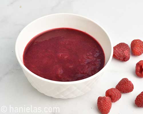 Raspberry puree in a white dish with fresh raspberries next to the bowl.