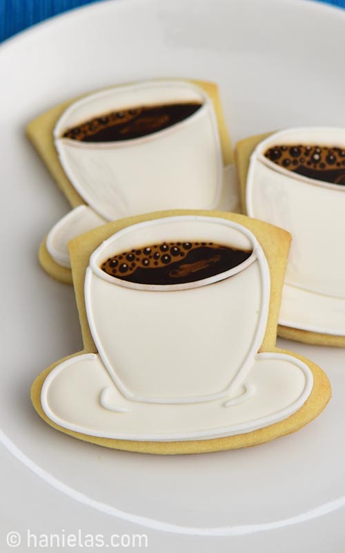 Royal icing decorated coffee cup shaped cookie on a plate.
