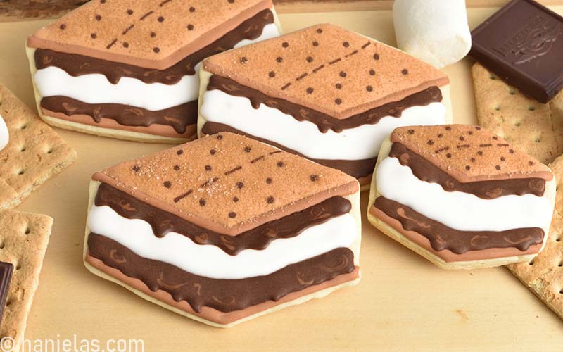 Decorated sugar cookies that look like s'mores displayed on a cutting board.