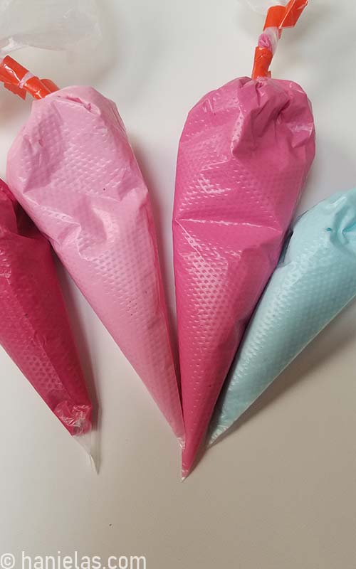 Blue, light pink, medium pink and dark pink royal icing in piping bags.