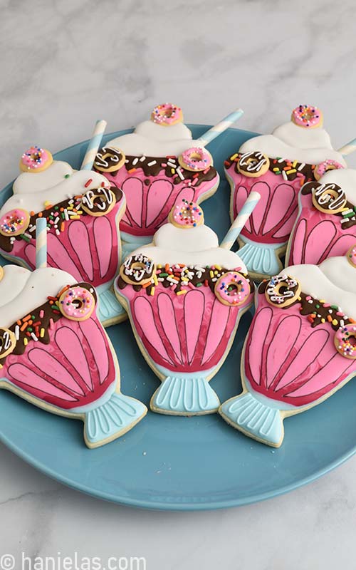 Cookies shaped like milkshakes decorated with royal icing displayed on a blue plate.