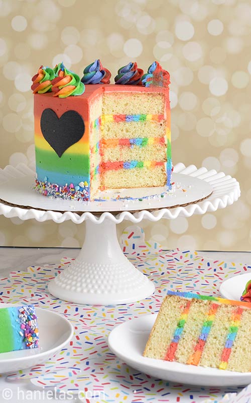 Cut cake showing rainbow buttercream layers on a cake stand.