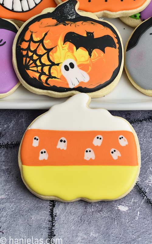Pumpkin cookie decorated with white, orange, yellow and small white ghosts.