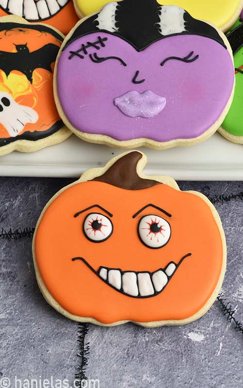 Pumpkin cookie decorated with scary eyes and white teeth.
