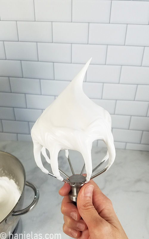 Hand holding a wire beater with a stiff meringue.