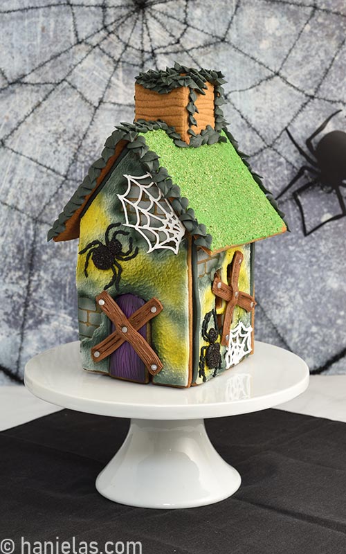 Halloween decorated gingerbread house displayed on a white cake stand.