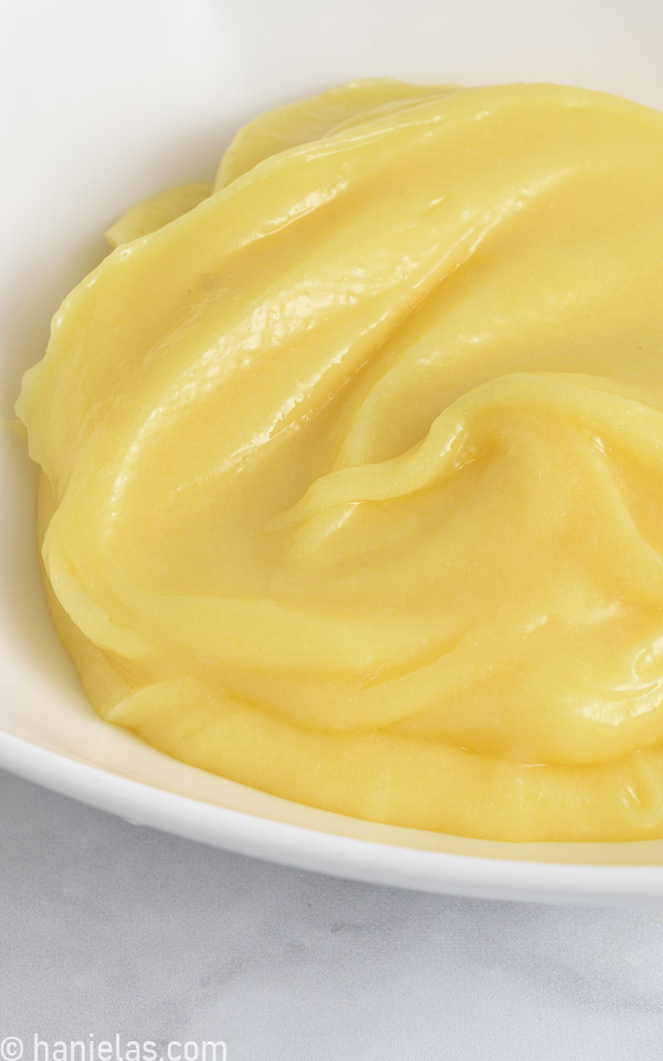 Detail of yellow lemon curd in a white bowl.