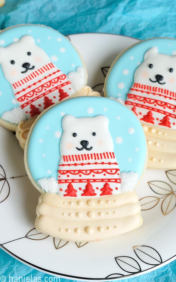 Snow globe cookies decorated with royal icing on a pretty white and silver plate.
